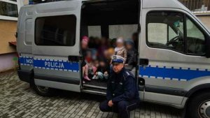 Umundurowany policjant stoi z dziećmi przy radiowozie
