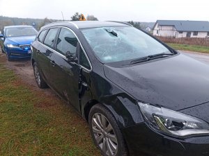 Rozbity samochód osobowy koloru czarnego i stojący za nim nieoznakowany radiowóz policji