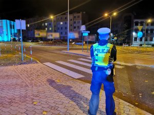Umundurowanych policjant stoi przy przejściu dla pieszych.  Pora nocna.