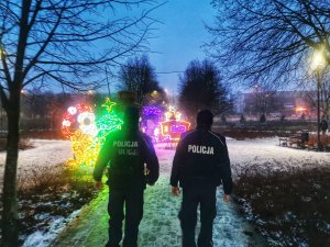 Dwóch policjantów idzie parkiem. W tle świąteczne ozdoby.