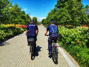 Dwóch policjantów jedzie przez park, obok siebie na rowerach.