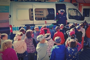 Policjant stojący przy radiowozie rozmawiający z dziećmi