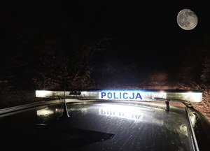Podświetlony napis policja na dachu radiowozu i w tle księżyc.