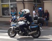 na zdjęciu widać jadącego na motorze funkcjonariusza policji w tle ludzi robiących zdjęcia