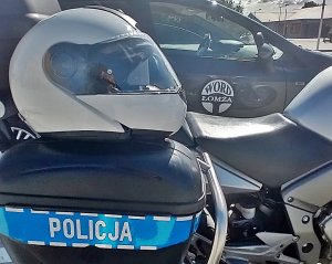 Biały kask motocyklowy na sakwie motocykla policyjnego, w oddali napis WORD Łomża na pojeździe egzaminacyjnym