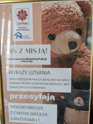 Ramka ze zdjęciem Miasia , logo caritas. Napis Miś z misją w Komendzie Miejskiej Policji w Łomży.