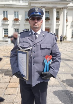 Policjant, który jest laureatem konkursu stoi przed budynkiem