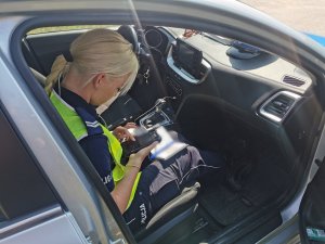 Umundurowana policjantka siedzi w radiowozie i sprawdza dokumenty kierowcy.