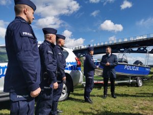 Komendant Miejski Policji w Łomży rozmawia z Prezydentem Miasta Łomża. Stoją przy policyjnej łódce na plaży miejskiej. Obok stoi trzech policjantów.