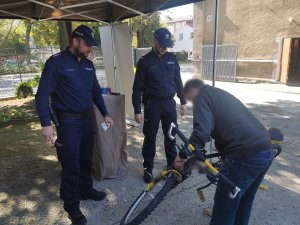 Umundurowani policjanci stoją obol mężczyzny, który trzyma rower do oznakowania.