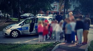 Policjant przy radiowozie mówi do grupki dzieci