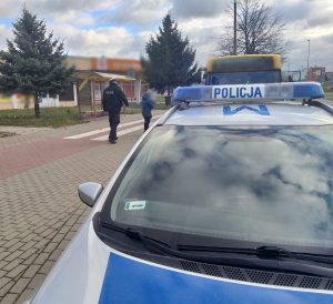 Umundurowany policjant kontroluje autobus MPK. Widoczny na pierwszym planie radiowóz policyjny.