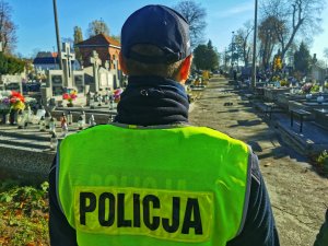 umundurowany policjant w kamizelce odblaskowej z napisem policja patroluje cmentarz.