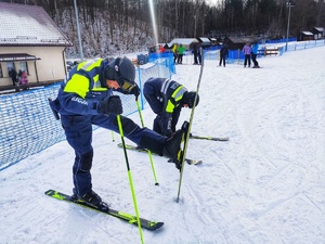 Dwóch umundurowanych policjantów z patrolu narciarskiego przeprowadza rozgrzewkę.