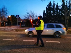 Umundurowany policjant zatrzymuje samochód do kontroli latarką koloru czerwonego