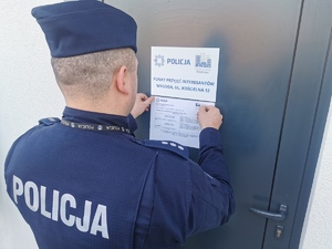 Naczelnik Prewencji Komendy Miejskiej Policji w Łomży przyklejaj szyld na drzwi, informujący o dzielnicowych.
