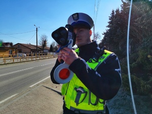 Umundurowany policjant mierzy prędkość pojazdom.