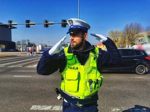 Umundurowany policjant kieruje ręcznie ruchem na skrzyżowaniu ulic.