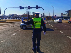 Umundurowany policjant kieruje ręcznie ruchem na skrzyżowaniu ulic.