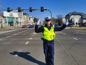Umundurowany policjant kieruje ręcznie ruchem na skrzyżowaniu ulic.