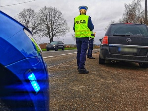 Dwoje umundurowanych policjantów w trakcie kontroli drogowej samochodu osobowego.