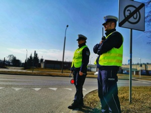 Dwóch umundurowanych policjantów stojących przy przejściu dla pieszych.