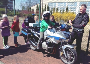 Dzieci ustawione w około policyjnego radiowozu. Obok policjant w stroju motocyklisty