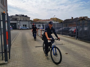 Dwóch policjantów na rowerach wyjeżdża z dziedzińca komendy na służbę.