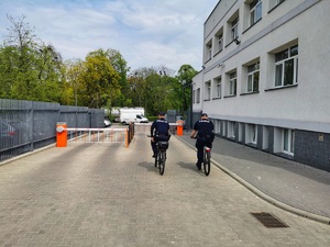 Dwóch policjantów na rowerach wyjeżdża z dziedzińca komendy na służbę.
