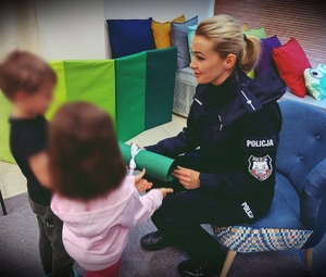 Policjantka siedząca na kolorowym fotelu odbiera od dzieci laurkę