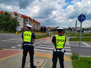 Dwóch umundurowanych policjantów stoi przy przejściu dla pieszych.