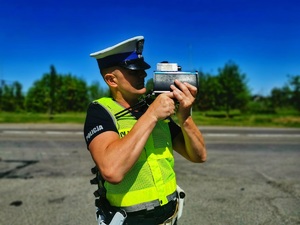 Umundurowany policjant mierzy prędkość pojazdom ręcznym miernikiem prędkości.