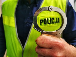 Policjant w kamizelce odblaskowej z napisem policja trzyma w ręku kajdanki.