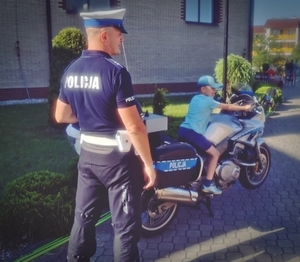 Policjant stojący obok motocykla służbowego. Na motocyklu siedzi dziecko