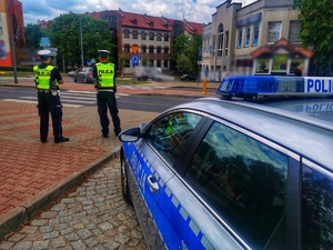 Policjanci stojący przy przejściu dla pieszych i przy radiowozie