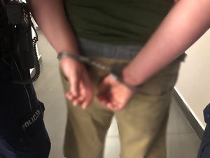 Mężczyzna z kajdankami założonymi na ręce trzymane z tyłu i obok fragment policyjnego munduru