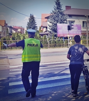 Policjant ruchu drogowego przeprowadza chłopca z rowerem przez przejście dla pieszych