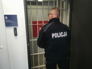 Policjant stoi przy kracie do pomieszczenia dla osób zatrzymanych.