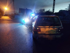 Zatrzymany samochód od kontroli drogowej, a przed nim zaparkowany radiowóz policyjny z włączonymi światłami błyskowymi.