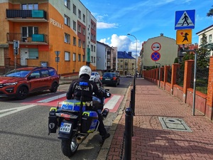 Policjant na motocyklu stoi przed przejściem dla pieszych.