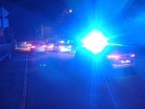 Dwa policyjne radiowozy z włączonymi światłami błyskowymi i zaparkowany przed nimi samochód osobowy
