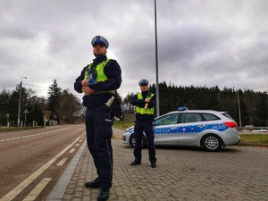 Dwóch umundurowanych policjantów stoi przy radiowozie