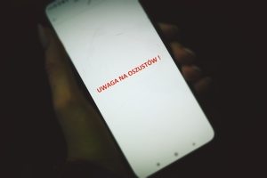dłoń trzymająca telefon z napisem uwaga na oszustów