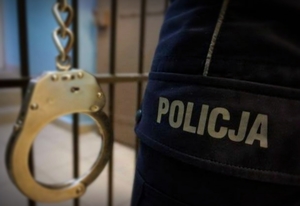 policjant trzyma kajdanki na tle krat